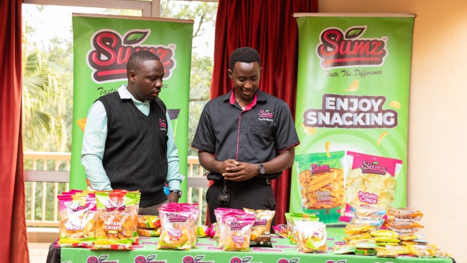 Two exhibitors standing behind a table of packaged snack products at an exhibition stand.